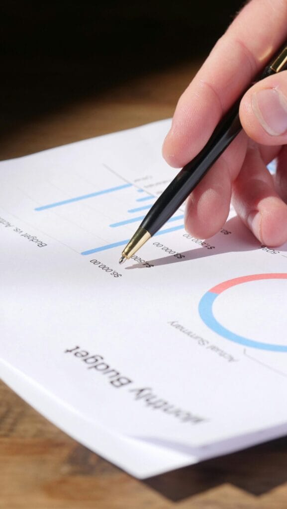 Close-up of an accountant's hand analysing data on a monthly budget document with graphs and charts.